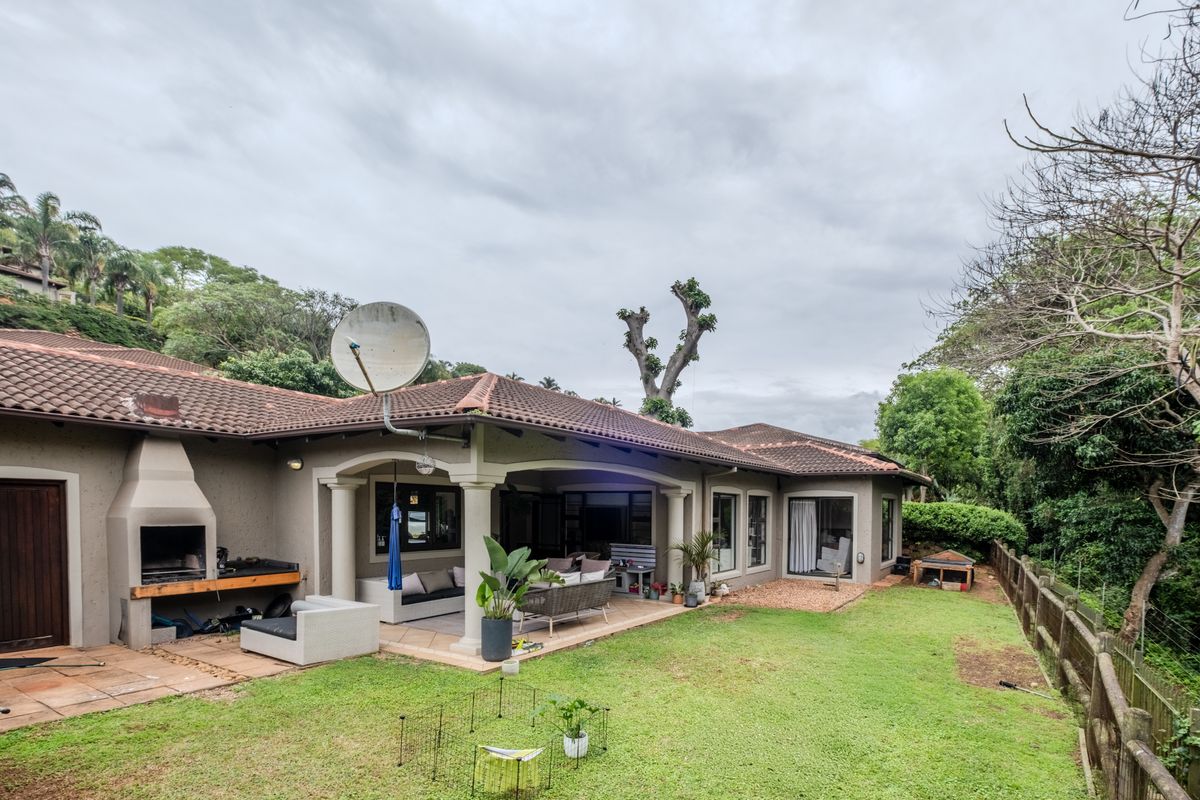 Rear view of the townhouse featuring a covered patio with a built-in braai, tiled roof, and a private garden area.