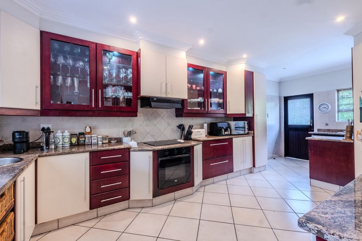 A well-maintained kitchen featuring two-tone cabinetry, granite countertops, built-in oven, electric hob, and tiled flooring with direct access to the exterior.