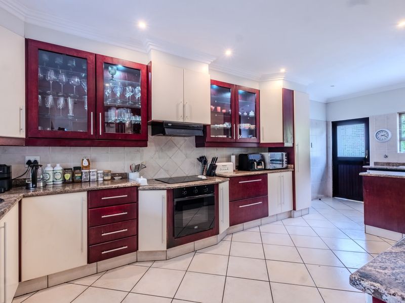 A well-maintained kitchen featuring two-tone cabinetry, granite countertops, built-in oven, electric hob, and tiled flooring with direct access to the exterior.