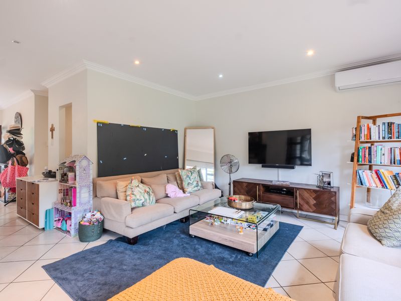 A bright and spacious living room featuring tiled flooring, recessed downlighting, and a wall-mounted air conditioning unit for climate control.