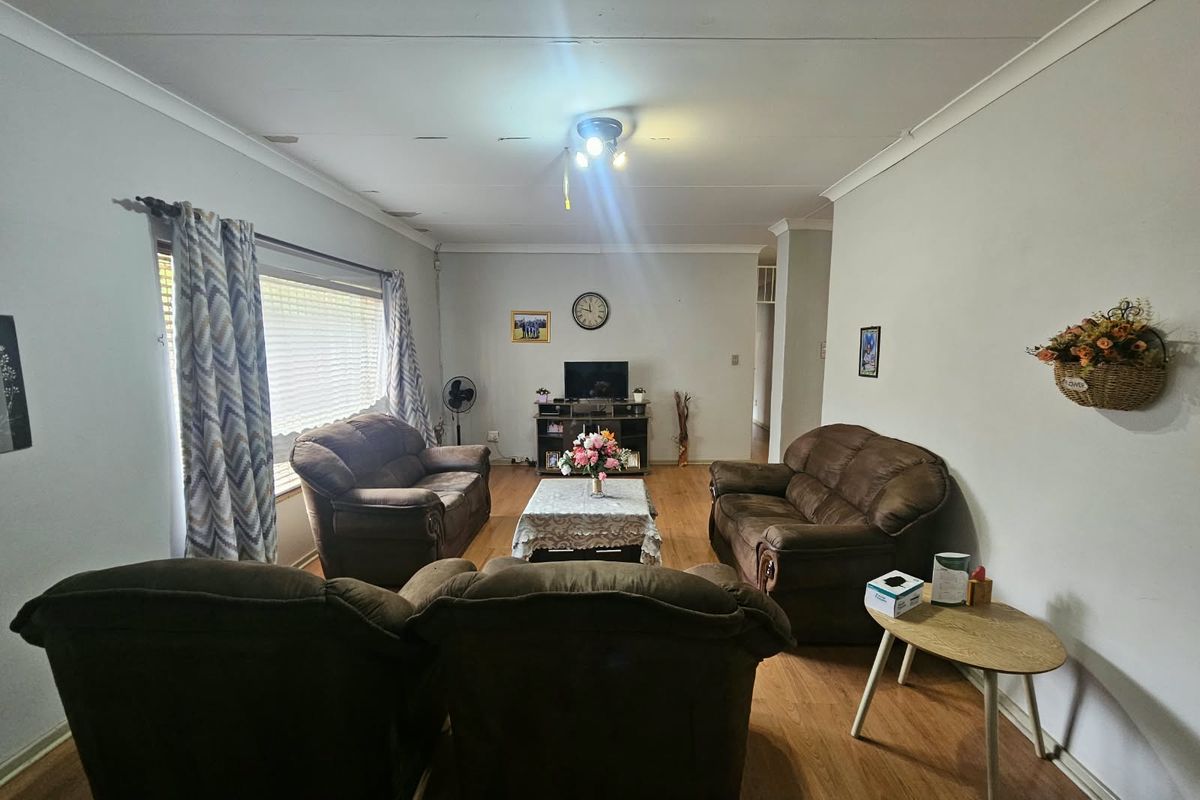 A living room featuring laminate flooring and ceiling coving, showing signs of wear on the ceiling surface.