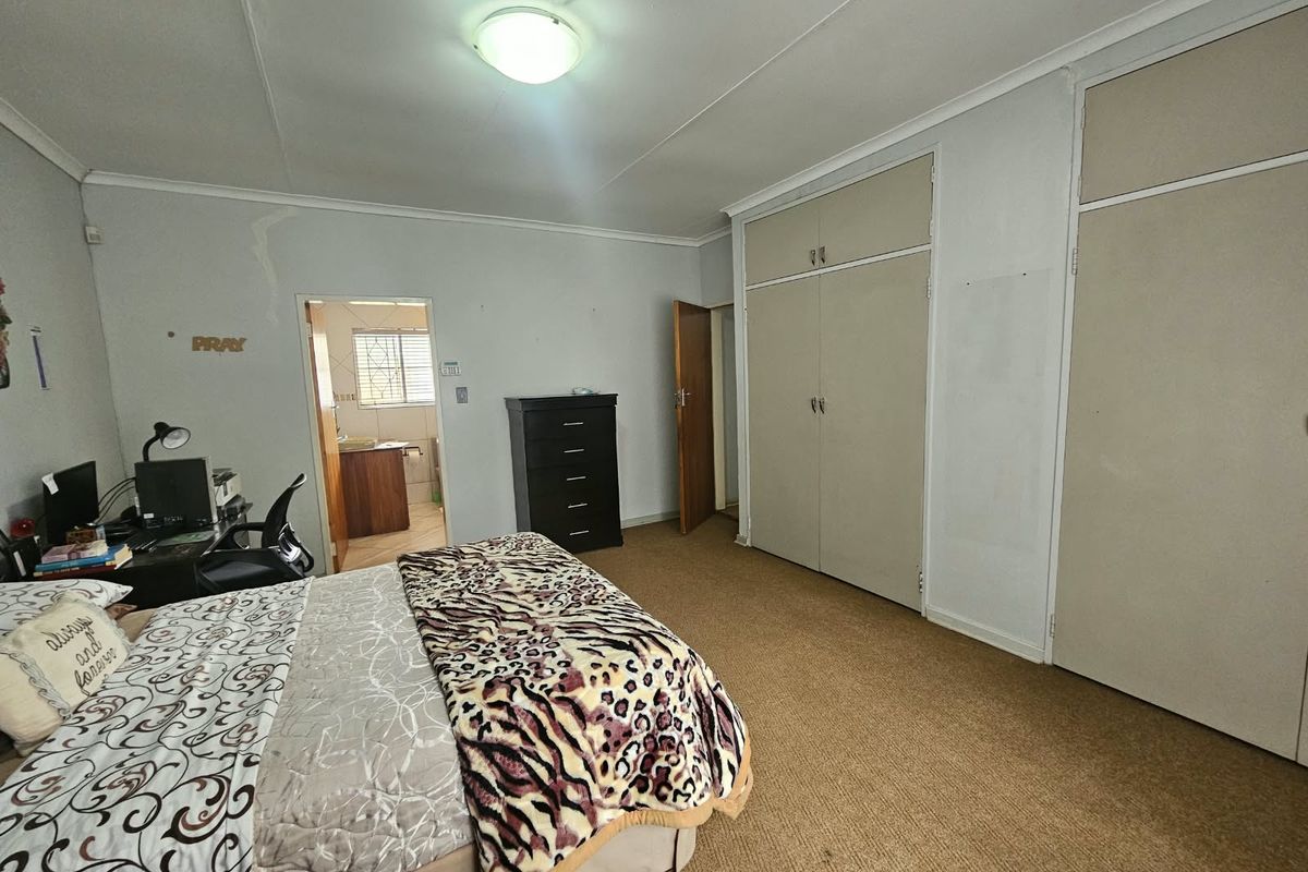 A spacious bedroom featuring built-in cupboards, carpeted flooring, and direct access to an adjacent room.