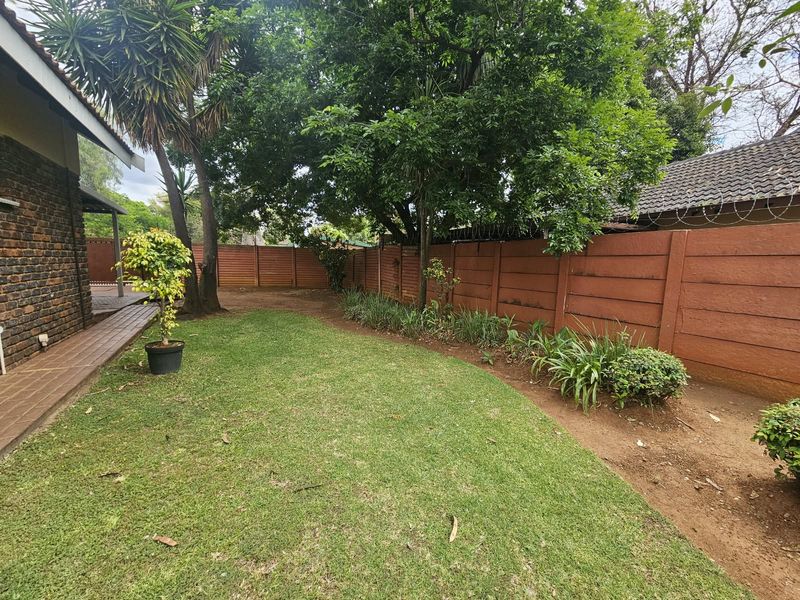 A private rear garden featuring a lawn, established trees, and a secure precast concrete boundary wall with razor wire.