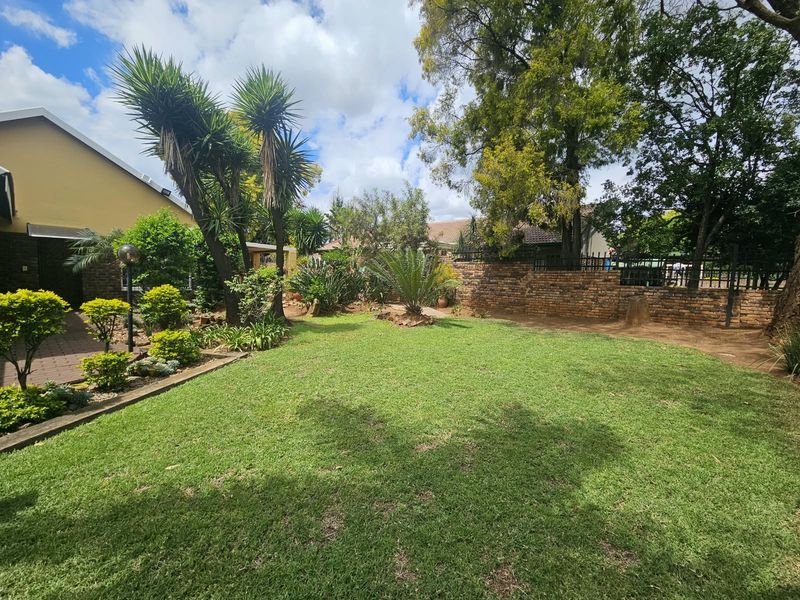A well-maintained private garden featuring a lush lawn, established trees, and a brick boundary wall, providing a peaceful outdoor space.