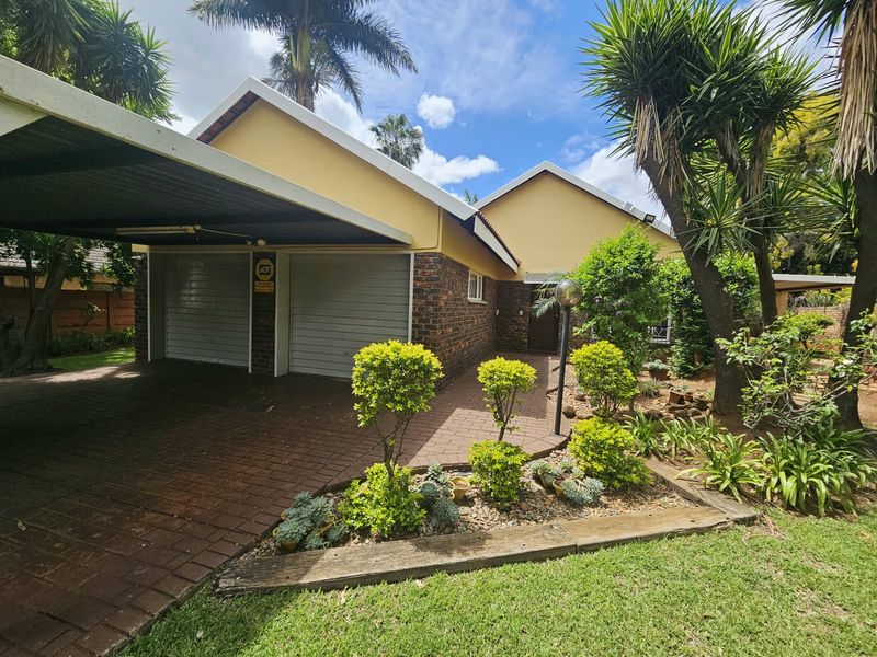 Front view of the property featuring a double garage, attached carport, paved driveway, and a well-maintained landscaped garden.