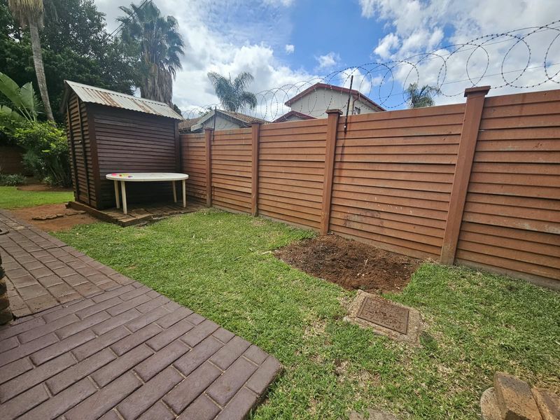 A rear garden area featuring timber boundary fencing with security razor wire, a paved walkway, and a small garden shed.
