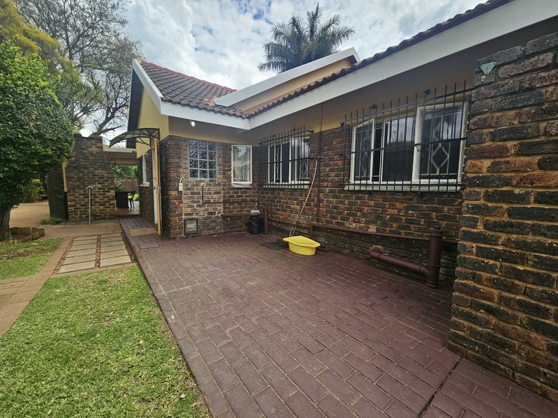 Rear exterior view of the house featuring face brick walls, a paved patio area, and security bars on the windows.