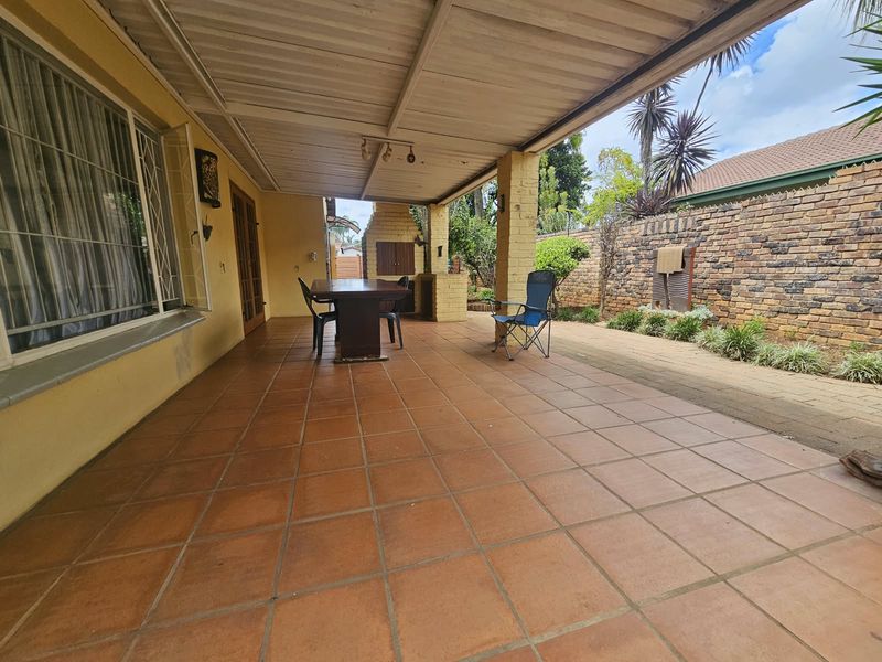 Spacious covered patio featuring a built-in braai, tiled flooring, and a brick boundary wall, offering a functional outdoor entertainment area.