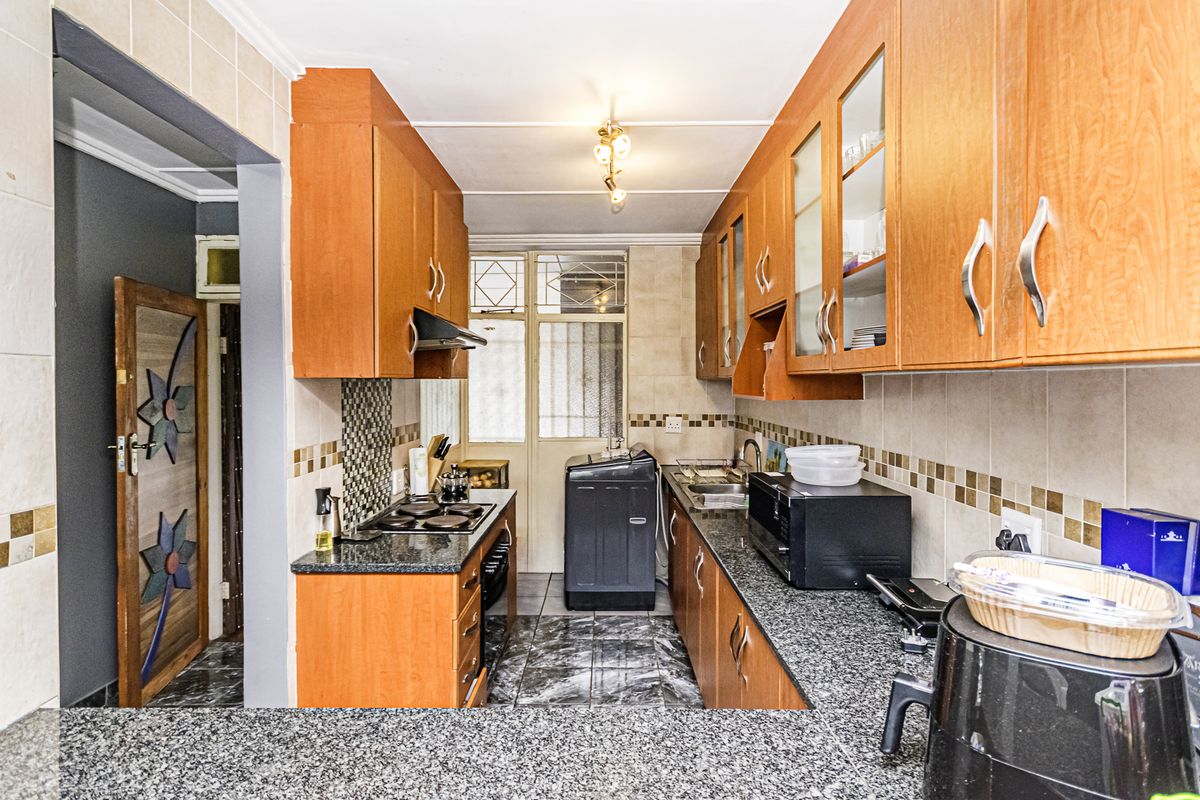 Functional kitchen featuring granite countertops, wooden cabinetry, built-in hob, extractor fan, and tiled finishes, offering a practical layout for daily meal preparation.