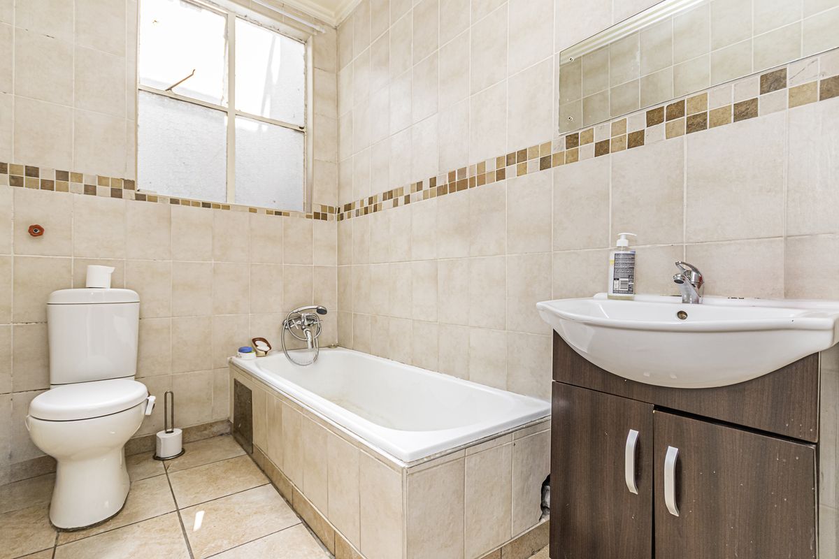 A dated bathroom featuring tiled walls and flooring, a built-in bathtub, a vanity cabinet with a basin, and a toilet.