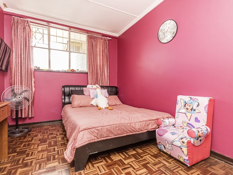 A bedroom featuring parquet flooring and a window with security bars, currently finished with vibrant pink wall paint.