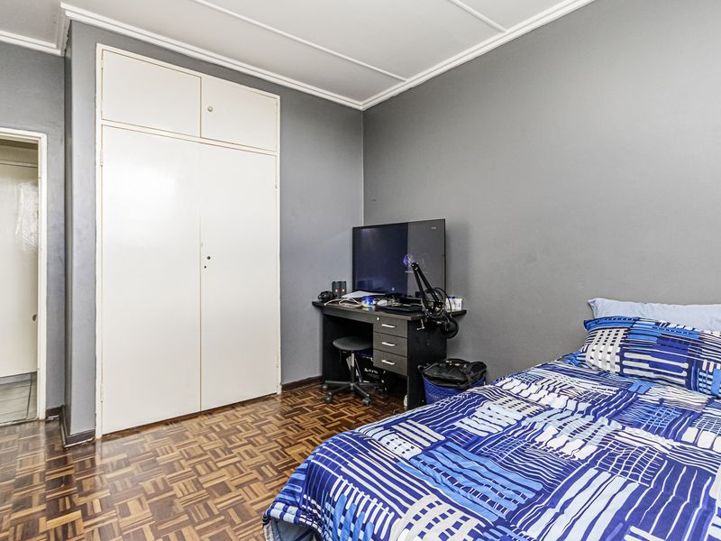 A bedroom featuring classic parquet flooring, a built-in wardrobe, and grey painted walls, offering a functional space with potential for modernization.