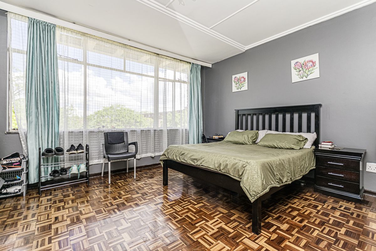 Spacious bedroom featuring classic parquet flooring, large windows allowing ample natural light, and decorative ceiling molding.