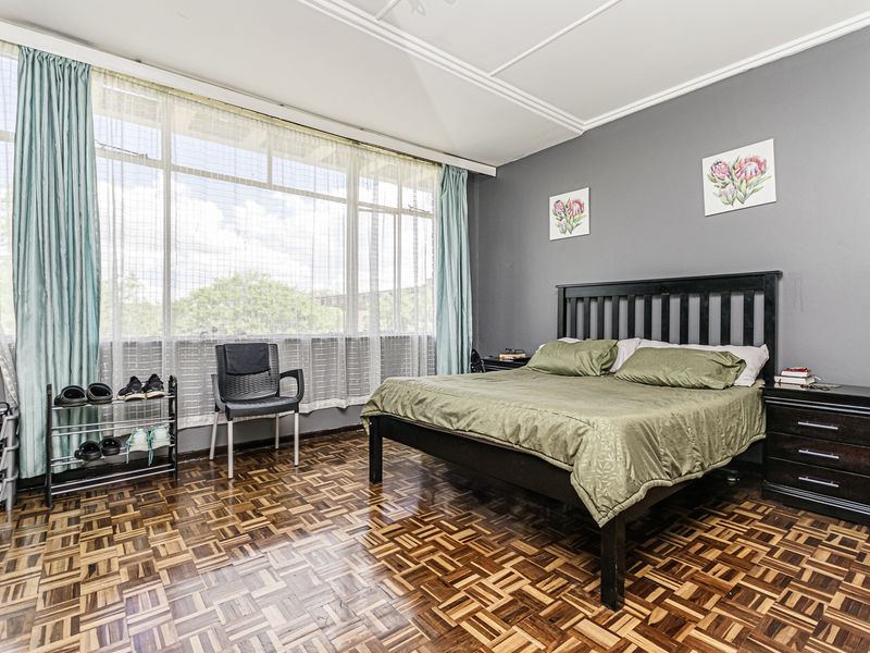 Spacious bedroom featuring classic parquet flooring, large windows allowing ample natural light, and decorative ceiling molding.
