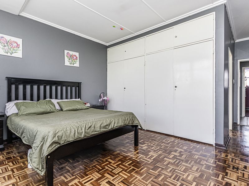 A spacious bedroom featuring classic parquet flooring, ample built-in cupboard storage, and neutral grey wall tones.