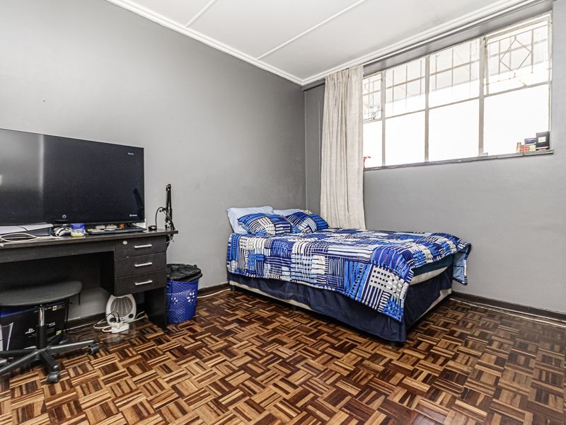 A bedroom featuring classic parquet flooring, grey painted walls, and a large steel-framed window with security bars.