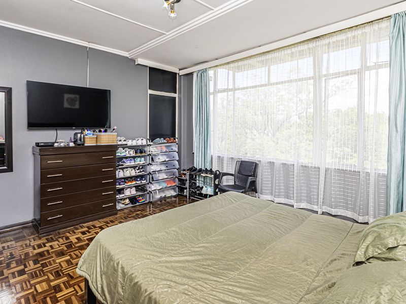 Spacious bedroom featuring classic parquet flooring and a large window with natural light, requiring some ceiling maintenance and cosmetic updates.