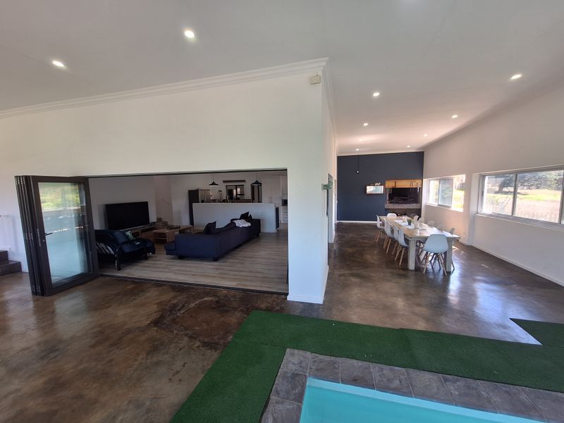 Spacious open-plan living and dining area featuring polished concrete floors, bi-fold doors opening to a pool area, and a built-in indoor braai.