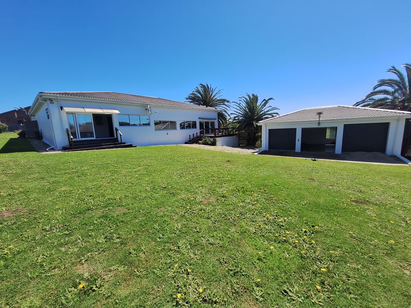 Spacious rear exterior view featuring a well-maintained lawn, a main house with sliding doors and a wooden deck, and a detached triple garage.