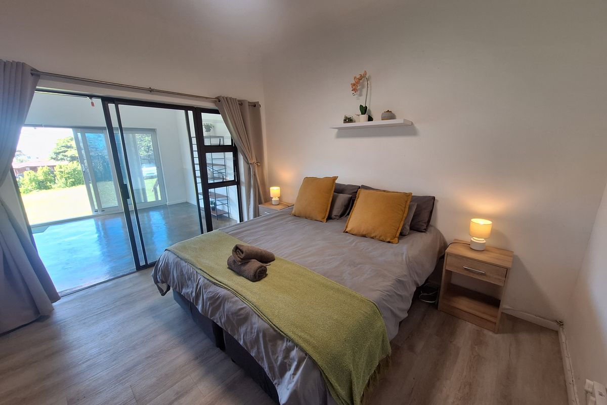 A well-lit bedroom featuring laminate flooring and a large sliding glass door that provides direct access to an outdoor patio area.