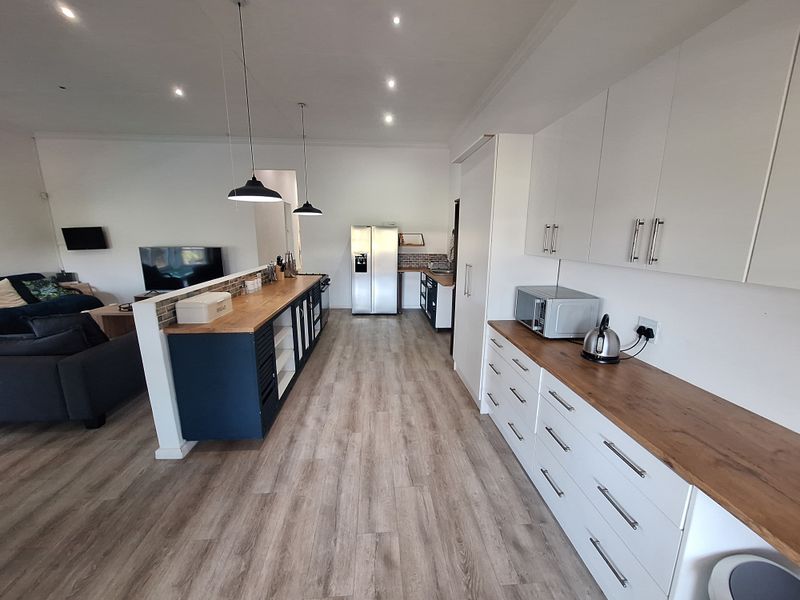 Modern open-plan kitchen and living area featuring sleek white and dark blue cabinetry, wooden countertops, and contemporary lighting fixtures.