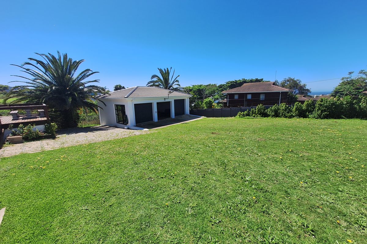 Spacious rear garden featuring a well-maintained lawn, a triple garage with tiled roof, and an adjacent timber deck area.
