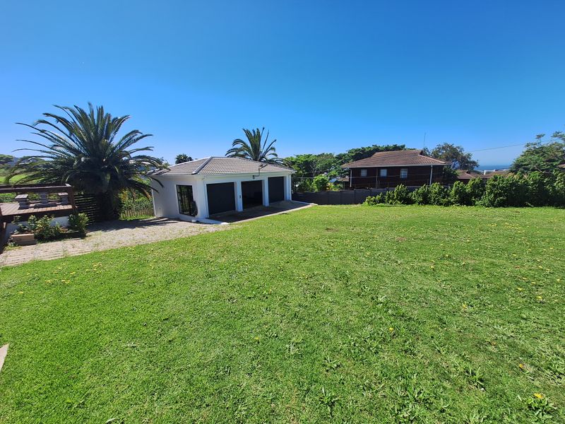 Spacious rear garden featuring a well-maintained lawn, a triple garage with tiled roof, and an adjacent timber deck area.