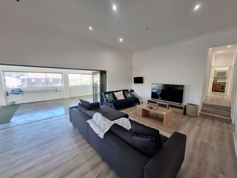 Spacious open-plan living area featuring modern laminate flooring, recessed downlights, and large bi-fold doors leading to an adjacent space.