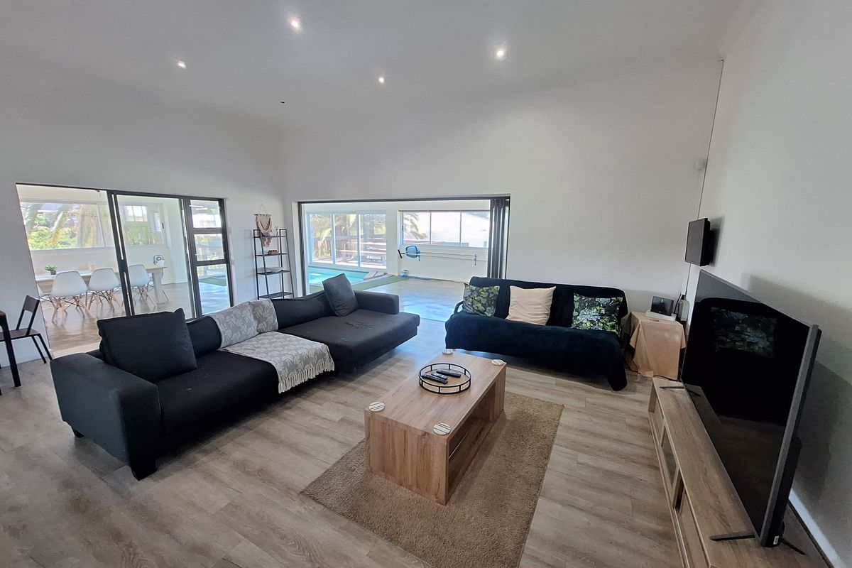 Spacious living room featuring modern laminate flooring, recessed downlighting, and large sliding glass doors that provide seamless access to the outdoor patio and pool area.