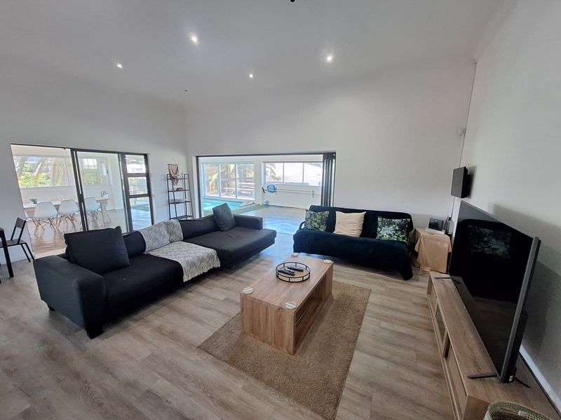 Spacious living room featuring modern laminate flooring, recessed downlighting, and large sliding glass doors that provide seamless access to the outdoor patio and pool area.