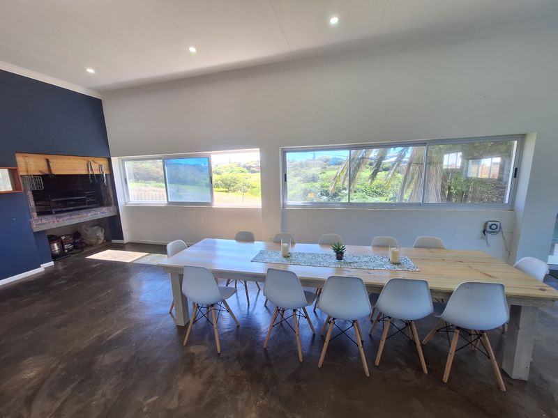 Spacious open-plan dining area featuring polished concrete floors, a built-in braai, and large sliding windows offering scenic garden views.