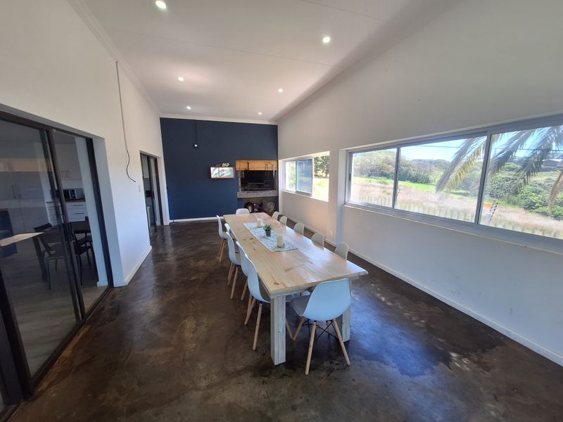 Spacious dining area featuring polished concrete floors, recessed lighting, and a built-in braai, with large windows offering scenic views.