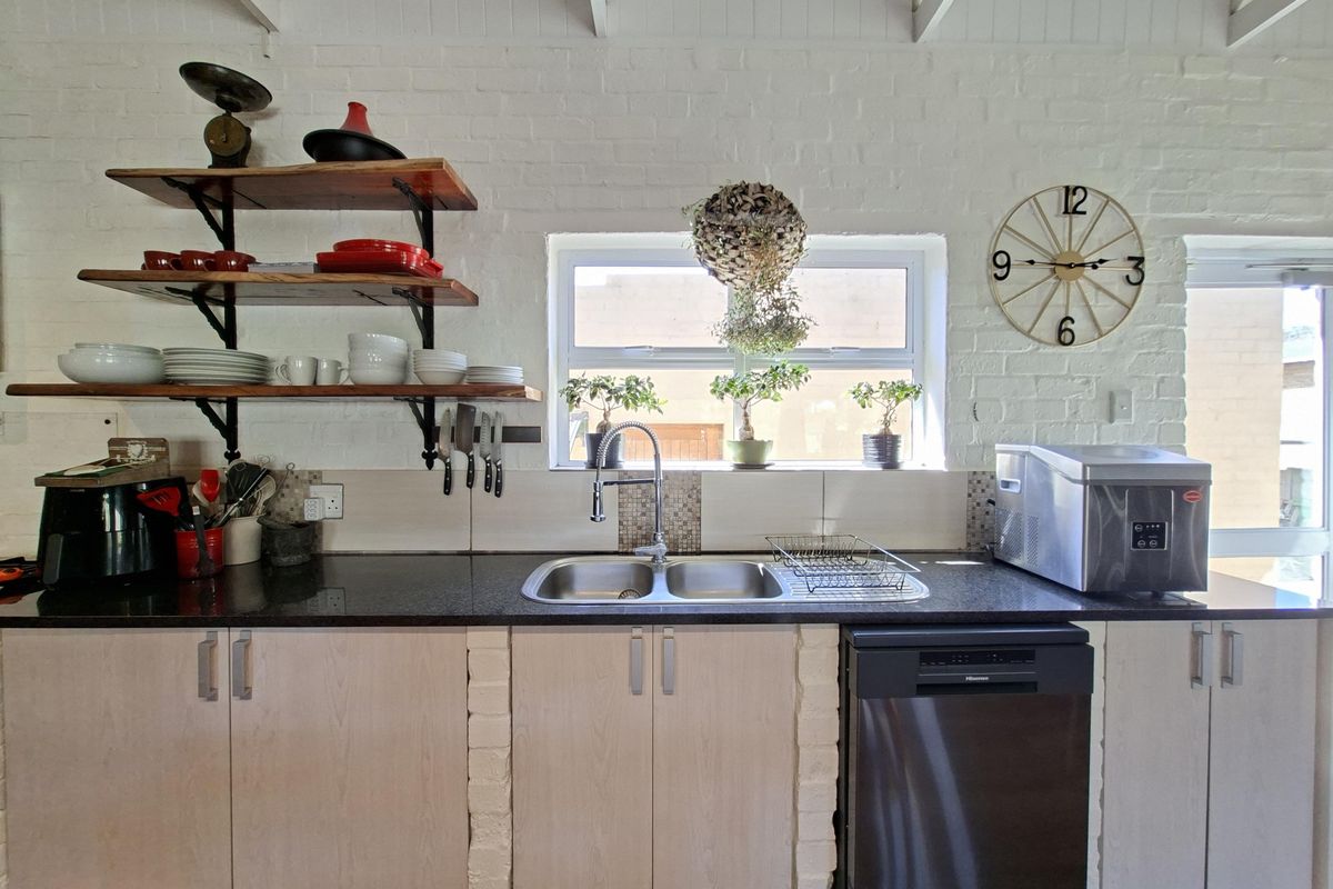 A bright kitchen featuring exposed brick walls, timber open shelving, granite countertops, and a double bowl sink with a modern mixer tap.