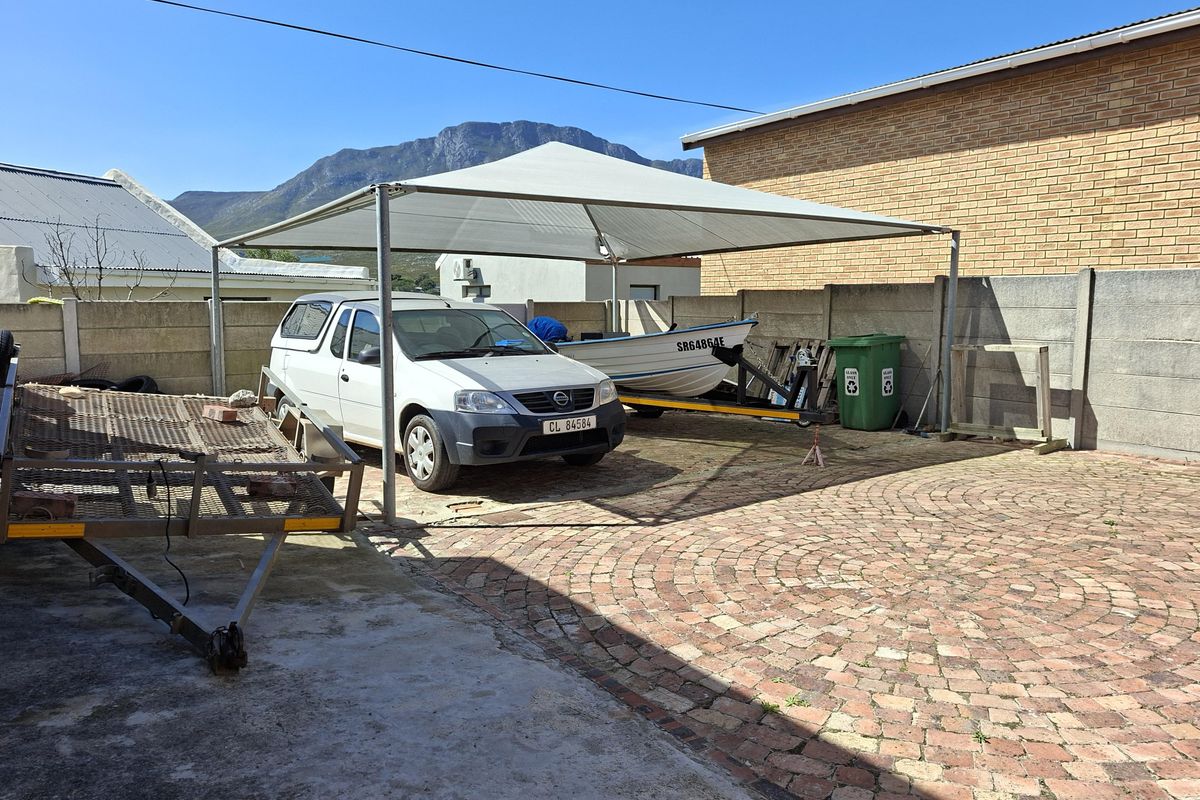 Rear exterior area featuring a paved driveway, precast concrete boundary wall, and a fixed shade sail structure.