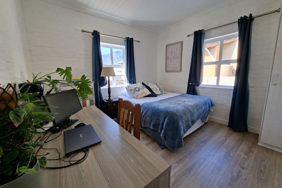 A cozy bedroom featuring painted brick walls, laminate flooring, and a tongue and groove ceiling, offering a bright and comfortable living space.