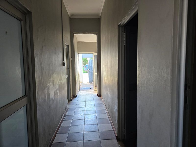 A narrow interior hallway featuring tiled flooring and multiple doorways, showing signs of wear and requiring cosmetic updates to the wall finishes.
