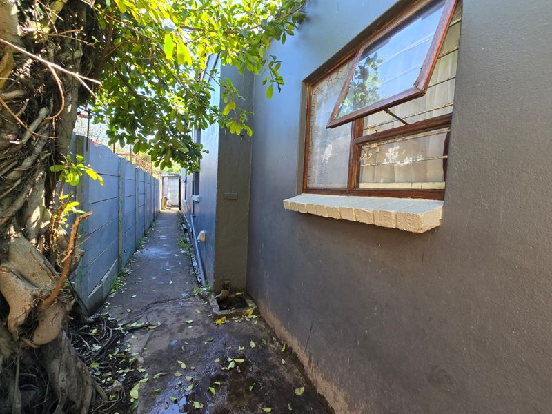 A narrow side passage of the property featuring a concrete boundary wall, paved walkway, and a window with security bars.