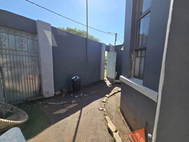 A side or rear exterior passage featuring a paved walkway, boundary wall, and metal security gate access.