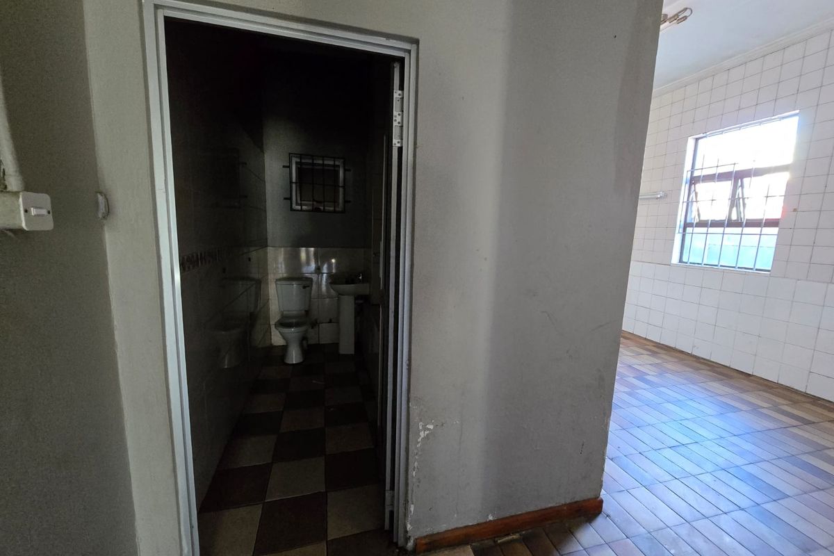 A small, vacant bathroom featuring a toilet and pedestal basin, with tiled flooring and walls, requiring cosmetic updates to improve its overall condition.