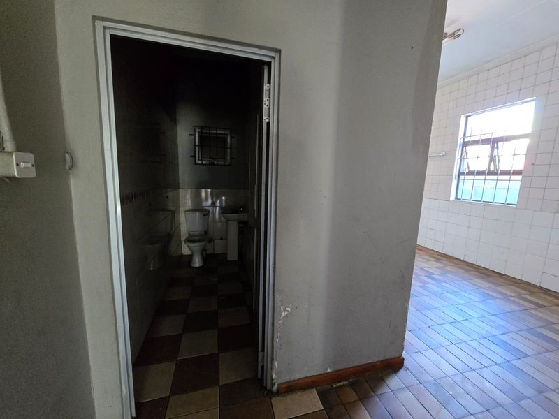 A small, vacant bathroom featuring a toilet and pedestal basin, with tiled flooring and walls, requiring cosmetic updates to improve its overall condition.