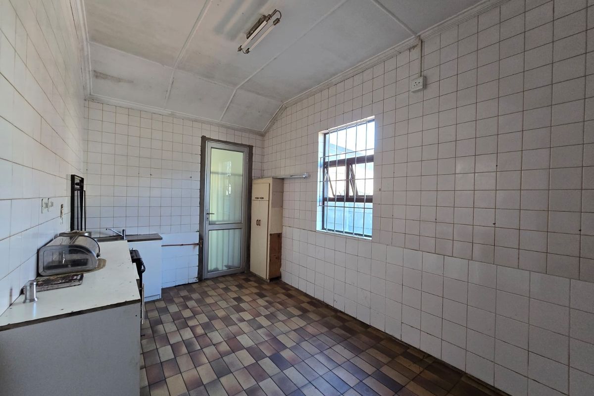 A dated kitchen featuring tiled walls and flooring, built-in cabinetry, and a security-barred window, offering a blank canvas for renovation.