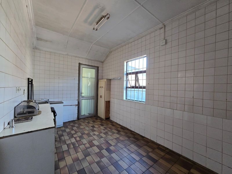 A dated kitchen featuring tiled walls and flooring, built-in cabinetry, and a security-barred window, offering a blank canvas for renovation.