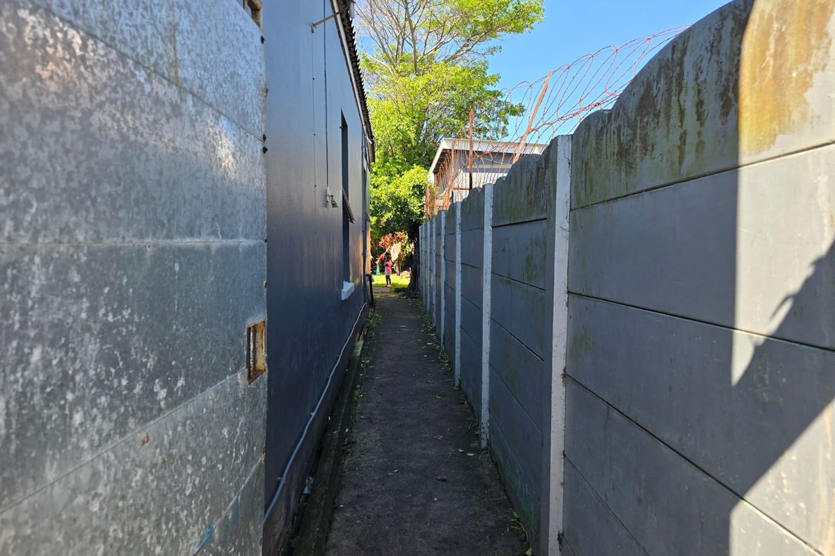 A narrow side passage between the house exterior and a precast concrete boundary wall topped with security razor wire.