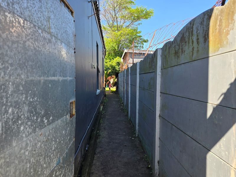 A narrow side passage between the house exterior and a precast concrete boundary wall topped with security razor wire.