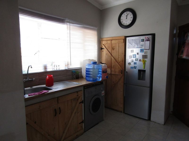 A functional laundry area featuring wooden cabinetry, a stainless steel sink, tiled flooring, and space for a washing machine.