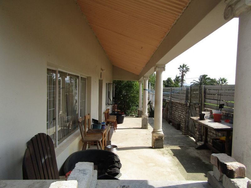 A covered patio area featuring concrete columns and a corrugated roof, providing an outdoor space with views of the side garden and boundary wall.
