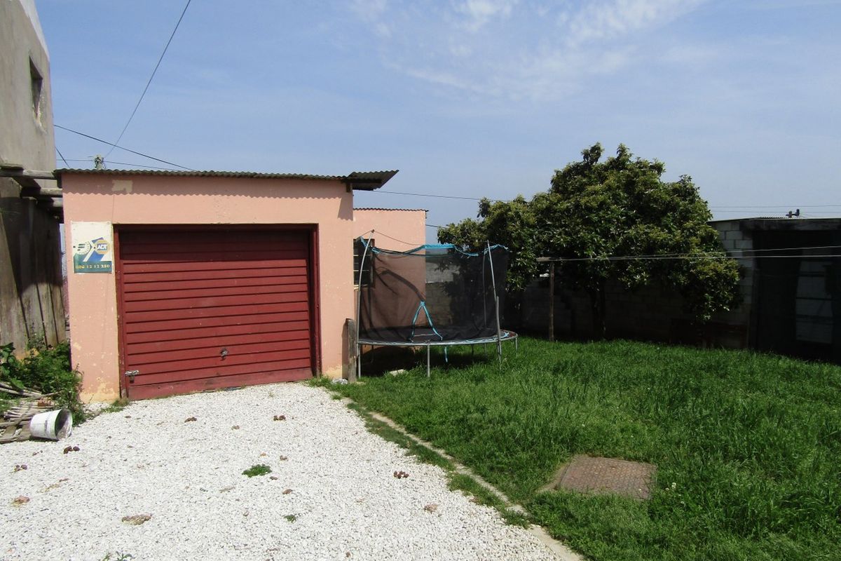 Rear exterior view featuring a single garage with a red roller door, gravel driveway, and a small grassed garden area.