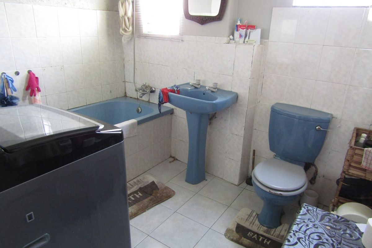 A dated bathroom featuring a blue pedestal basin, matching toilet, and built-in bathtub with ceramic wall and floor tiling.