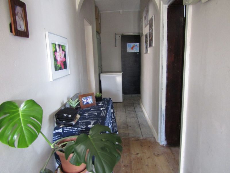 A narrow hallway featuring timber flooring and an arched transition, showing signs of wear and requiring cosmetic updates.