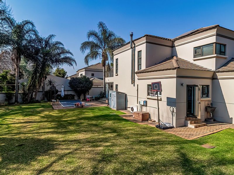 Rear view of the property featuring a spacious lawn, paved patio area, and a swimming pool, set within a private garden.